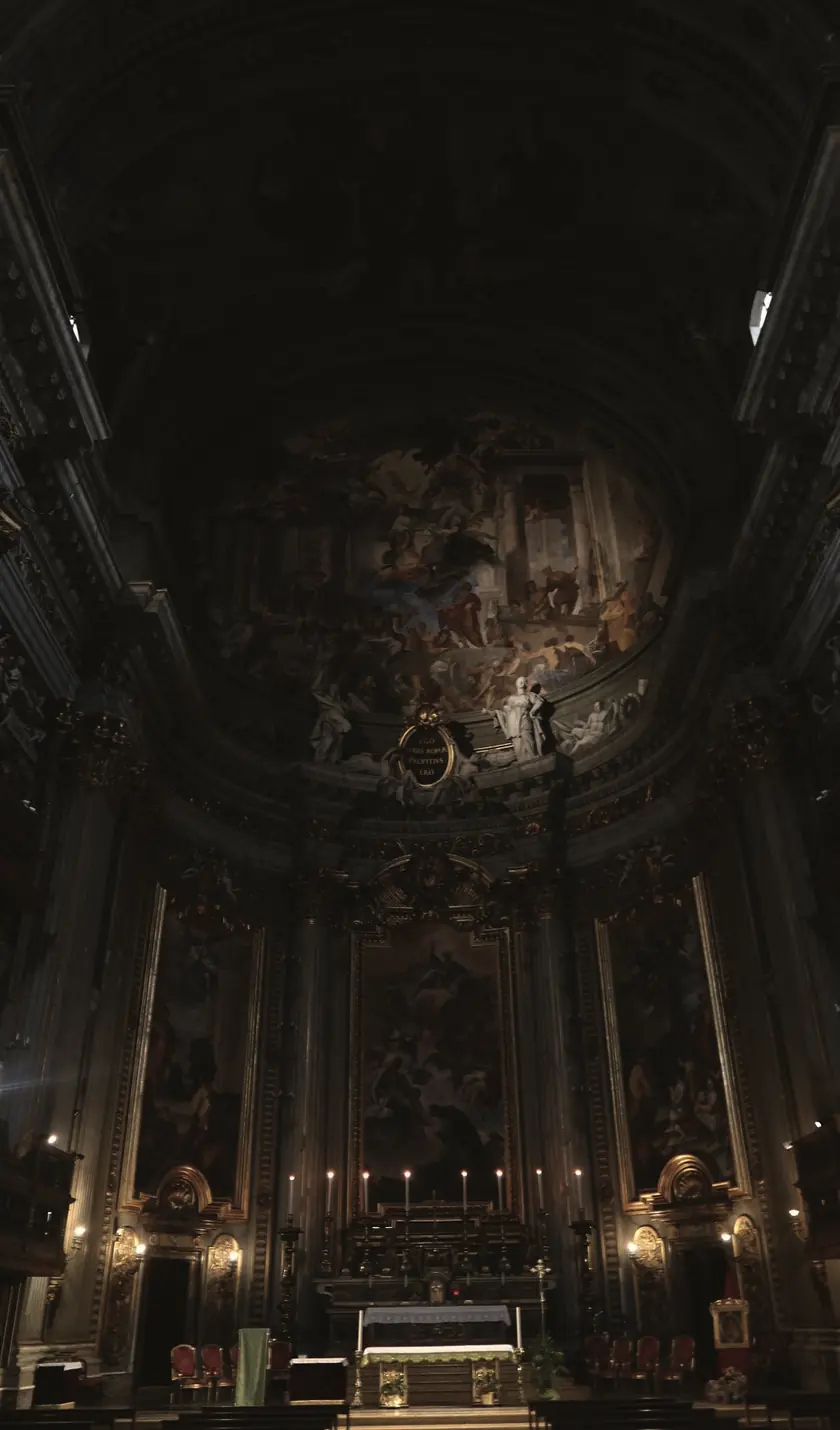 The interior of a Baroque church, looking down the nave: a painted vault overhead, a frescoed apse, and candles burning at the high altar.